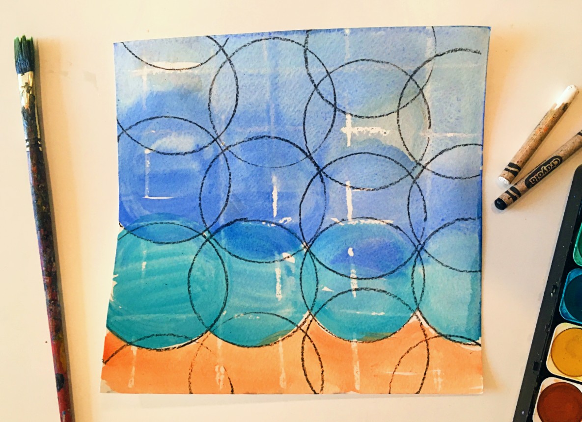 A blue, teal, and orange watercolor painting with black circles and white lines, surrounded by a paintbrush, crayons, and watercolor paints.