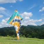 A large, outdoor sculpture that resembles a flowing piece of fabric with geometric designs in shades of blue, yellow, orange, and white.