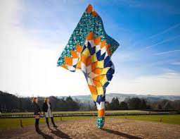 A large, outdoor sculpture that resembles a flowing piece of fabric with geometric designs in shades of blue, yellow, orange, and white.