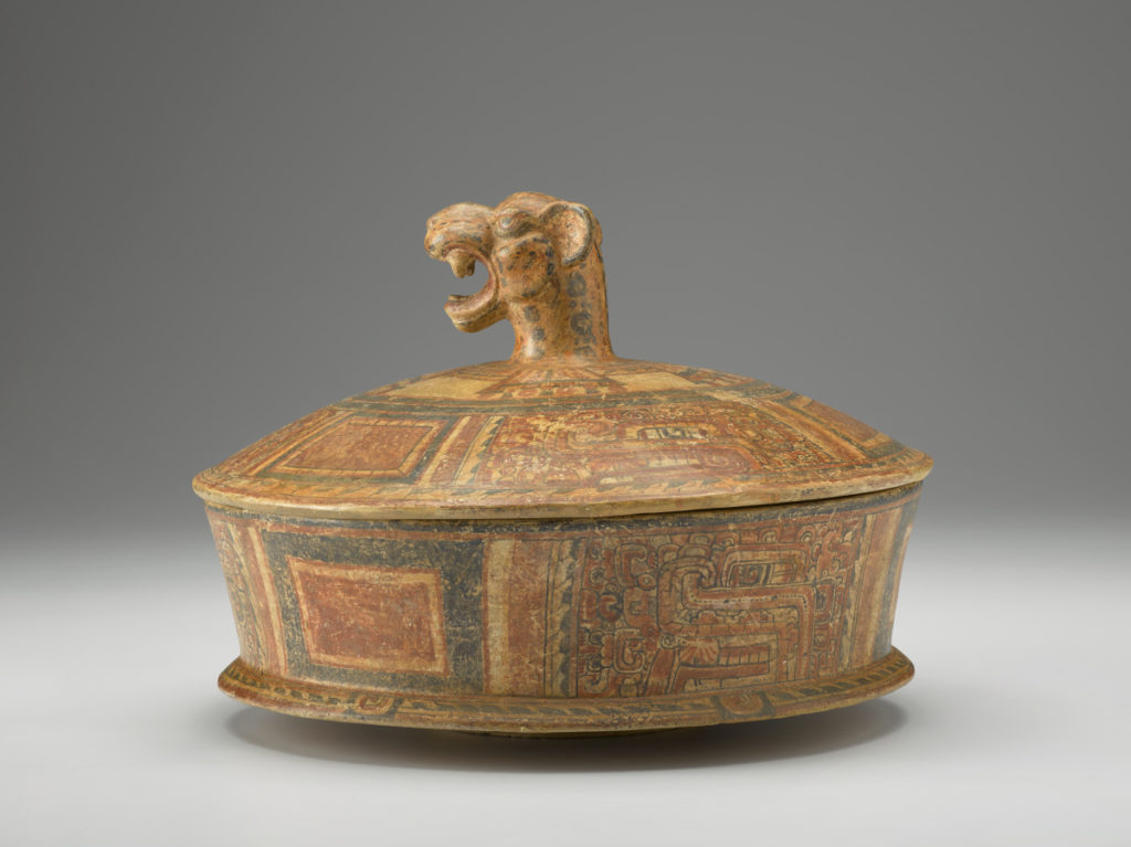 A painted terra-cotta dish with jaguar-head handle on top of the lid.