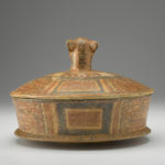 Rear view of a terracotta cylindrical dish with a lid that has a jaguar-head handle.