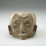 Front view of a light tan clay jar with a humanlike wrinkled face.