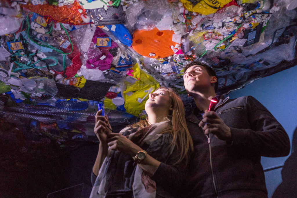 los visitantes miran una obra de arte hecha con plásticos recuperados