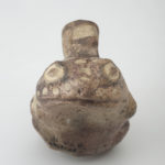 A ceramic vessel shaped like a frog, with a handle connecting the top of the frog’s head to a spout on its back.