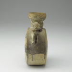 A ceramic vessel featuring a pair of monkeys with their hands covering their mouths. Their tails curve upward and connect with the neck of the vessel, serving as handles.