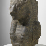 A granite sculpture of the upper torso, chest, and shoulders of a woman and the head of a lioness. Alternate view.