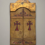 An image of a closed golden triptych with two red crosses painted on each of its two doors.