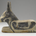 A wooden sculpture of a seated, black-and-white painted bull. Side view.