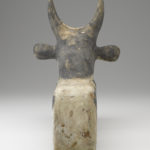 A wooden sculpture of a seated, black-and-white painted bull. Reverse view.