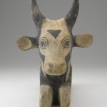 A wooden sculpture of a seated, black-and-white painted bull. Alternate view.