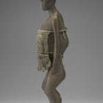 A small wooden sculpture of a woman with most of her torso covered by a burlap cloth. Side view.