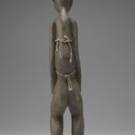 A small wooden sculpture of a woman with most of her torso covered by a burlap cloth. Reverse view.