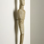 A white marble sculpture of a reclining female figure with her arms folded beneath her chest, set against a solid white background. Side view.