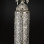 A hinged wooden case with domed finials on top and metallic floral patterns on the outside surface. Reverse view.