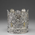 Una corona de plata cubierta de intrincados detalles, incluyendo diseños florales y texto hebreo.