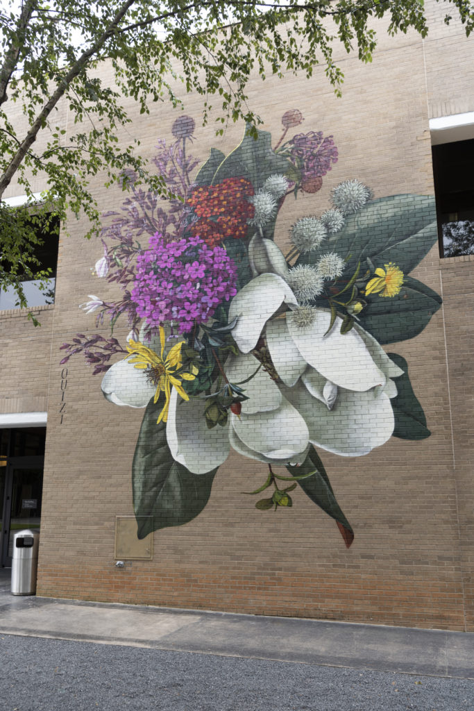 Un mural a gran escala de flores blancas, amarillas y rosas pintado sobre un edificio de ladrillo.