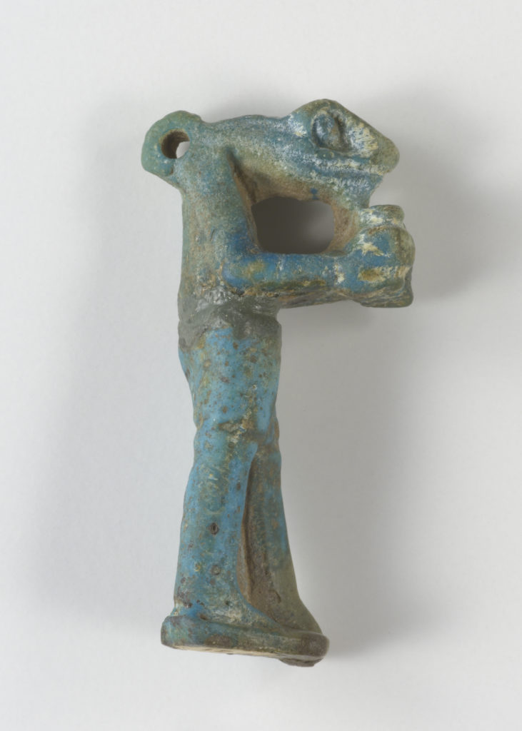 A small, blue-green sculpture depicting a snake-headed man wearing a kilt and holding an offering jar in front of his chest. There is a loop at the back of the figure’s head.