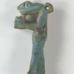 A small, blue-green sculpture depicting a snake-headed man wearing a kilt and holding an offering jar in front of his chest. There is a loop at the back of the figure’s head. Alternate view.