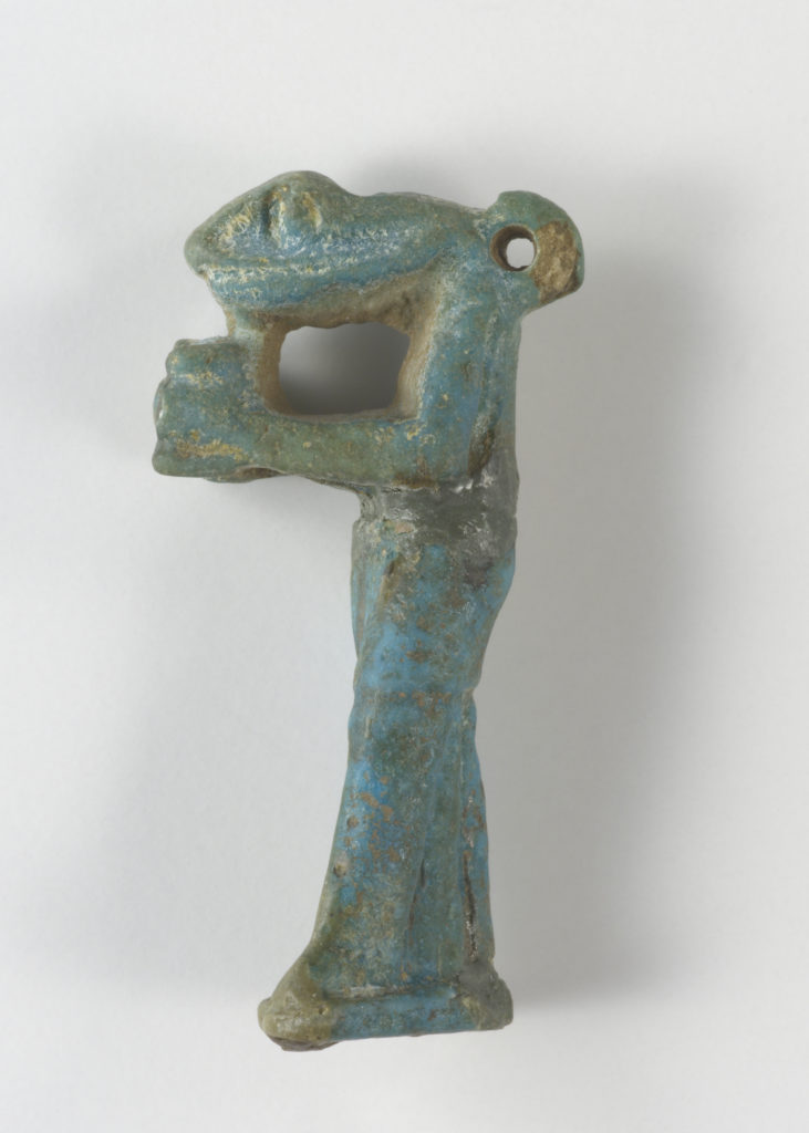 A small, blue-green sculpture depicting a snake-headed man wearing a kilt and holding an offering jar in front of his chest. There is a loop at the back of the figure’s head.