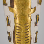 A white, linen-wrapped mummy covering with a gold Egyptian mask and gold accents on the chest, legs, and feet. Close up of leg coverings.