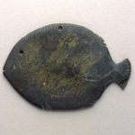A dark gray, fish-shaped object with carved fins at the top and bottom.