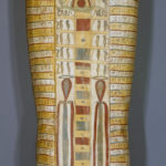 A wooden coffin shaped like a human body, with ancient Egyptian symbols and deities painted on its surface. View of reverse.