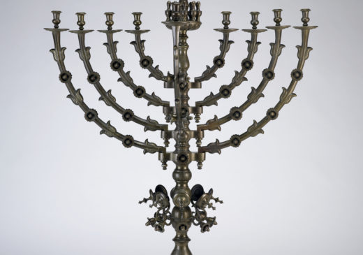 A copper Hanukkah menorah with an elaborate base and a gold eagle emblem at the top.