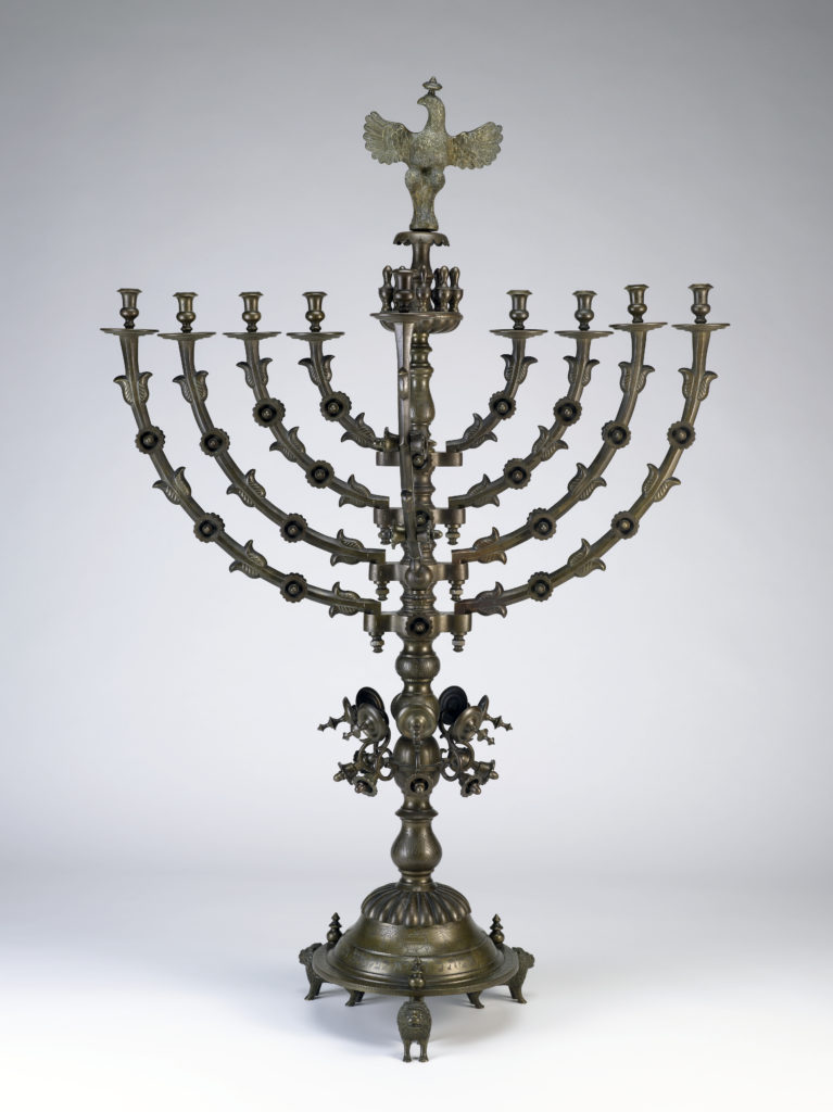 A copper Hanukkah menorah with an elaborate base and a gold eagle emblem at the top.