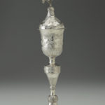 A silver goblet featuring intricate floral patterns and a flower blossom design at the top. Alternate view.