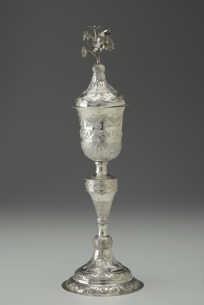 A silver goblet featuring intricate floral patterns and a flower blossom design at the top.