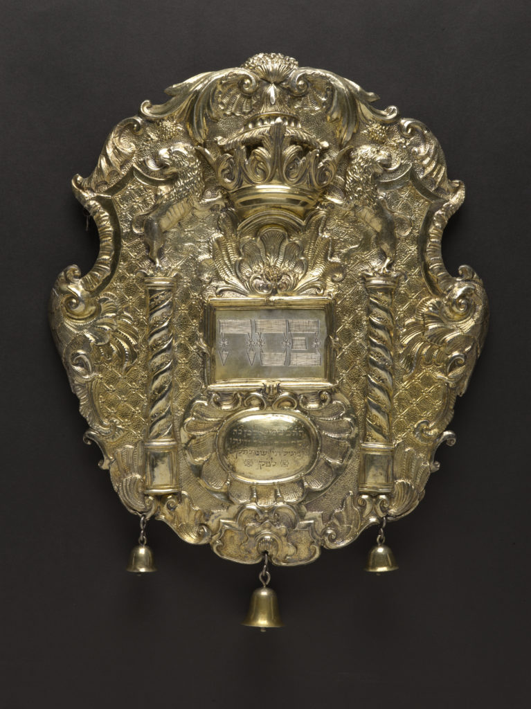 Escudo dorado con imágenes de una corona y dos columnas, con tres pequeñas campanas colgando del borde inferior.
