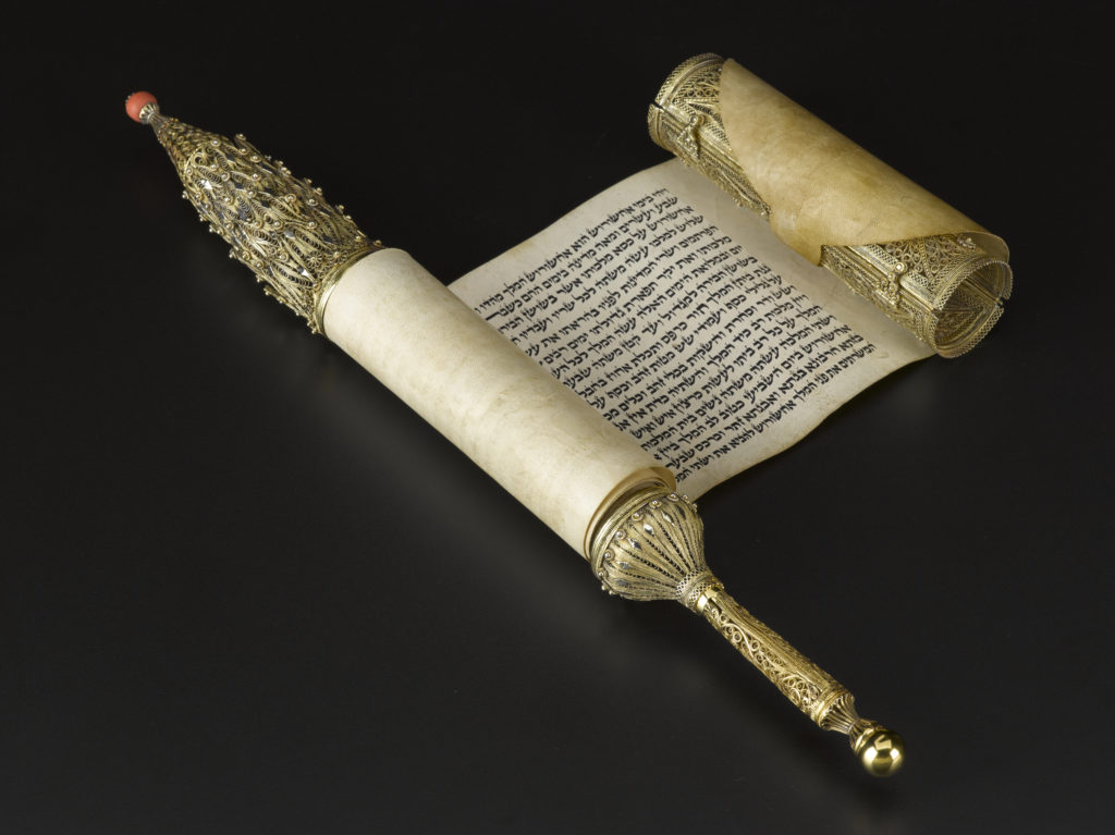 A detailed, cylinder-shaped gold case featuring a coral bead at one end and a handle on the other. Closed view.