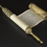 A detailed, cylinder-shaped gold case featuring a coral bead at one end and a handle on the other. Open view.