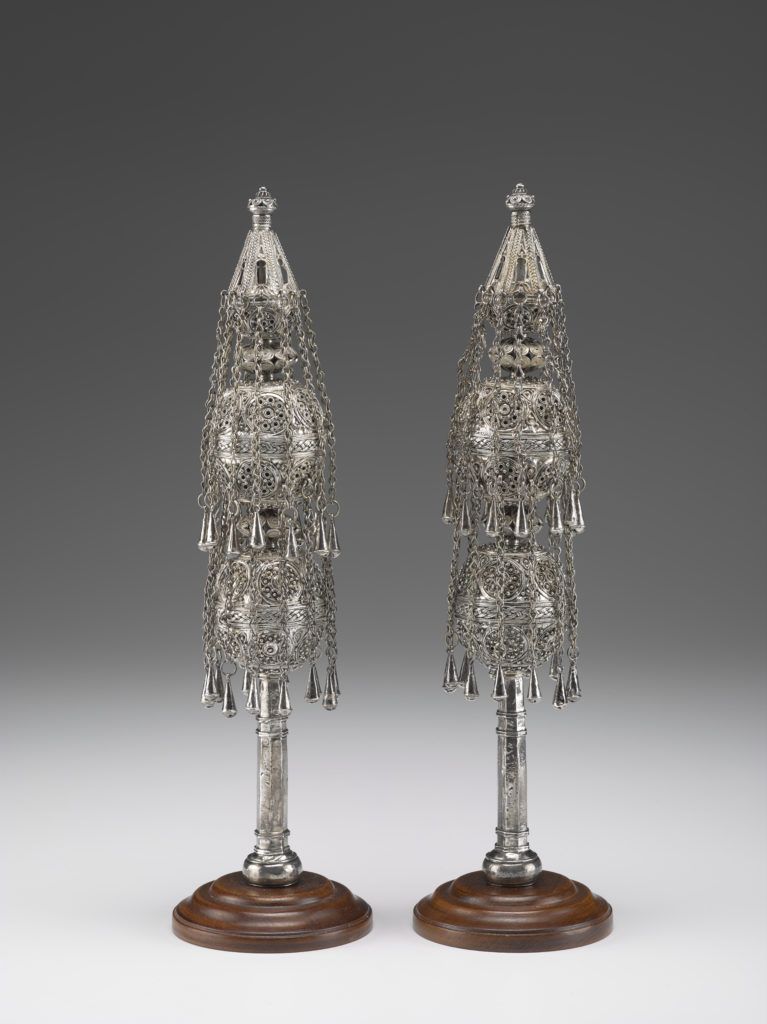 A pair of matching silver Torah finials featuring silver chains decorated with small bells.