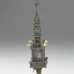 A silver filigree tower featuring two gold flags on the center section and a gold deer figure at the top. View of reverse.