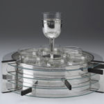 A silver-and-glass serving set of plates and dishes, with a wine glass on top.