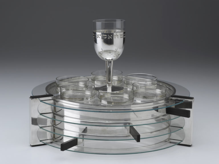Juego de platos y fuentes de plata y cristal, con una copa de vino encima.