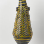 A small, dark-blue glass vessel with yellow designs. The vessel is long with a rounded bottom. It has two small rectangular handles on either side of the neck and a lipped opening.