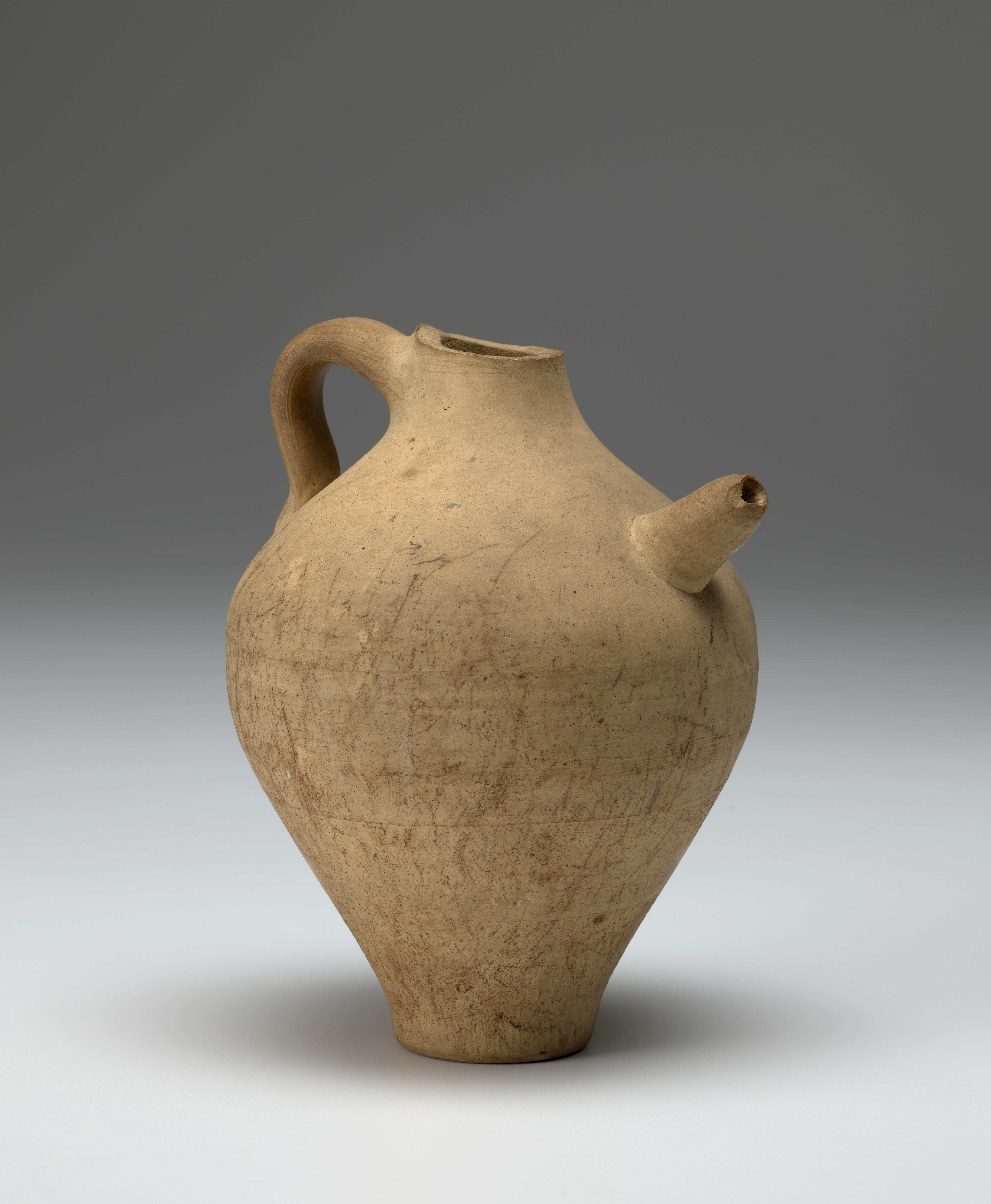 A yellow-beige ceramic jar with a handle and a spout.