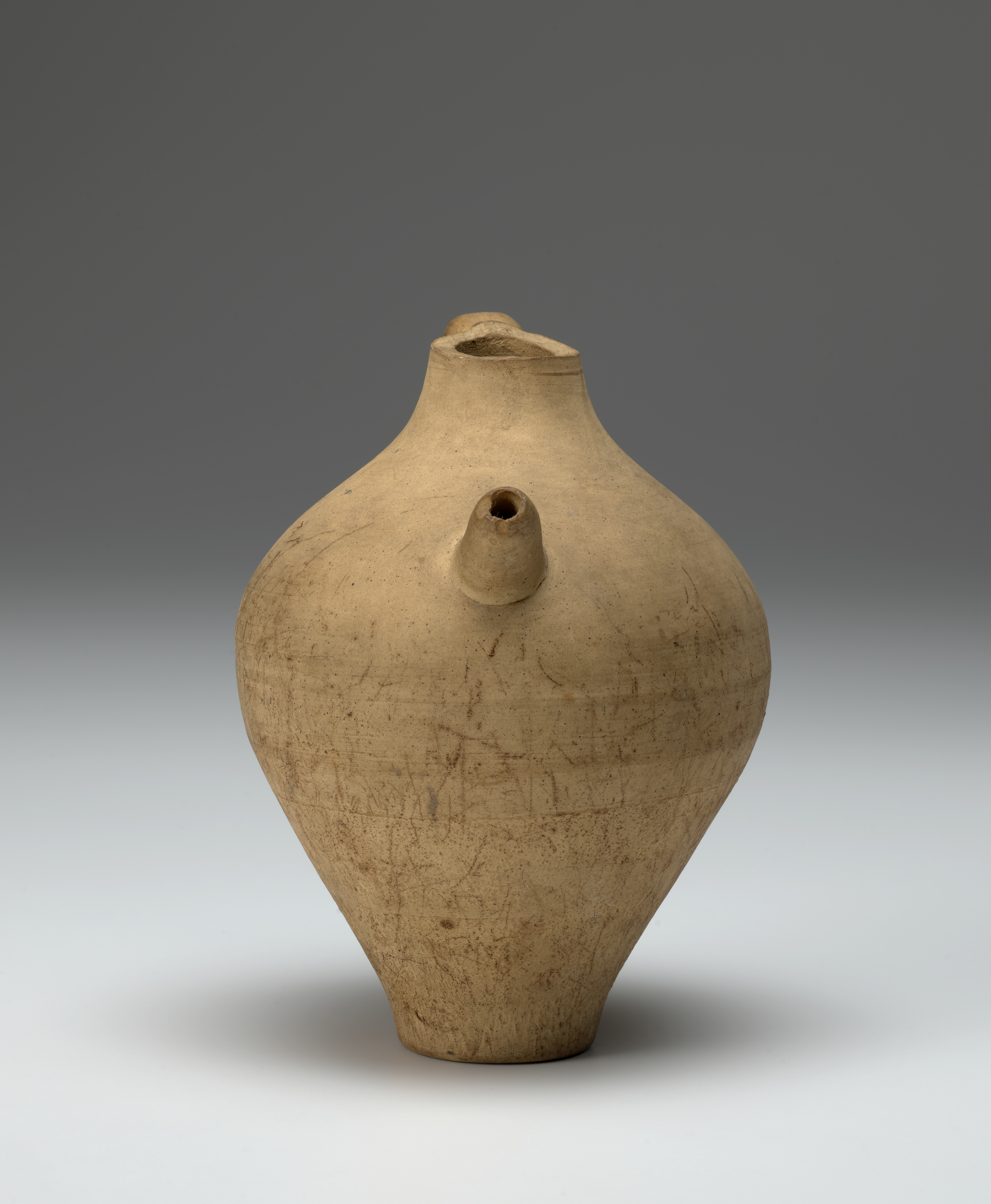 A yellow-beige ceramic jar with a handle and a spout.