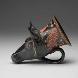 A black vase in the shape of a bull’s head, with a handle at the bottom and painted designs on the surface. Side view.