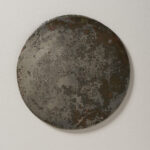 A round, gold-colored metal disk with a cloudy surface from aging.