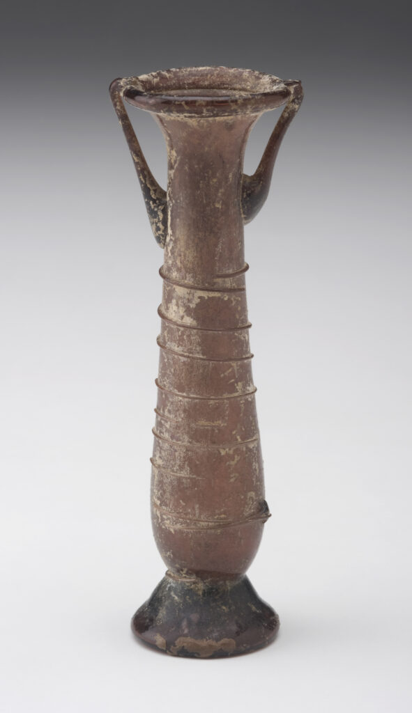 A tubular glass vessel with a long neck and two small handles. The vessel is a brownish-purple color and is decorated with a ribbon of glass that spirals around its neck. It has a flared base and a small opening.