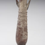 A tubular glass vessel with a long neck and two small handles. The vessel is a brownish-purple color and is decorated with a ribbon of glass that spirals around its neck. It has a flared base and a small opening. View of reverse.