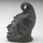 A small, black ceramic lantern in the shape of a man’s head wearing a cone-shaped hat. The face has deep wrinkles. There are holes in the eyes and under the ears, and the mouth is wide open. Side view.
