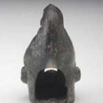 A small, black ceramic lantern in the shape of a man’s head wearing a cone-shaped hat. The face has deep wrinkles. There are holes in the eyes and under the ears, and the mouth is wide open. View of reverse.