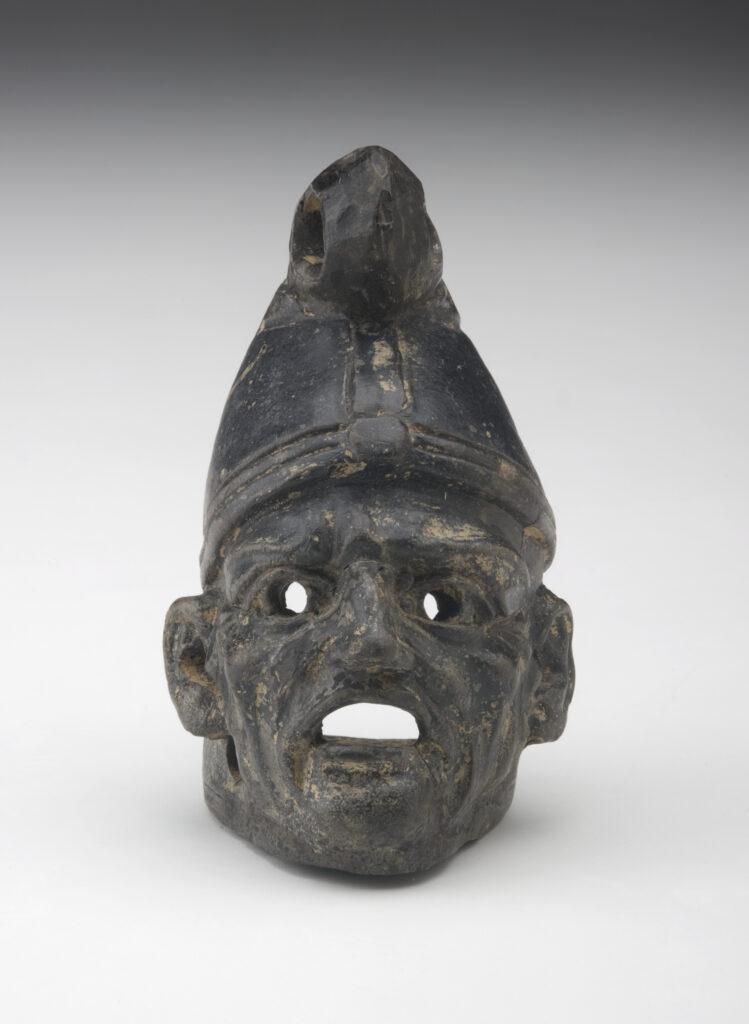 A small, black ceramic lantern in the shape of a man’s head wearing a cone-shaped hat. The face has deep wrinkles. There are holes in the eyes and under the ears, and the mouth is wide open.