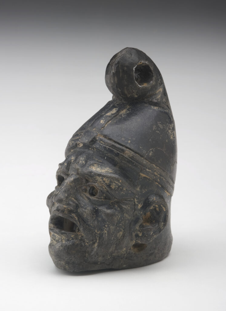 A small, black ceramic lantern in the shape of a man’s head wearing a cone-shaped hat. The face has deep wrinkles. There are holes in the eyes and under the ears, and the mouth is wide open.