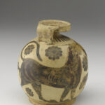 A beige-colored clay pot with a round base, a small neck, a handle, and flat mouth. It is decorated with black painted designs of flowers, a dolphin, and geometric shapes.