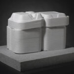 A white marble sculpture of open Styrofoam takeout boxes stacked on top of a gray, rectangle-shaped base.